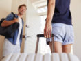 A young couple walking out the door of their apartment with luggage in hand, ready for the vacation of a lifetime.