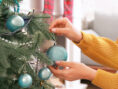 Woman hangs ornaments on a Christmas tree.