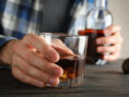Man holds glasses and bottle of whiskey on wooden background, close up