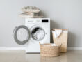 Washing machine with throw pillows on top and rattan laundry hampers to the right.