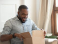 Man excitedly opens a package inside his apartment.