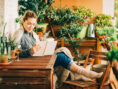 Young woman enjoys a good book and a glass of wine from the comfort of her dreamy balcony garden.