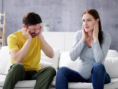 Two people sitting on white couch covering their ears